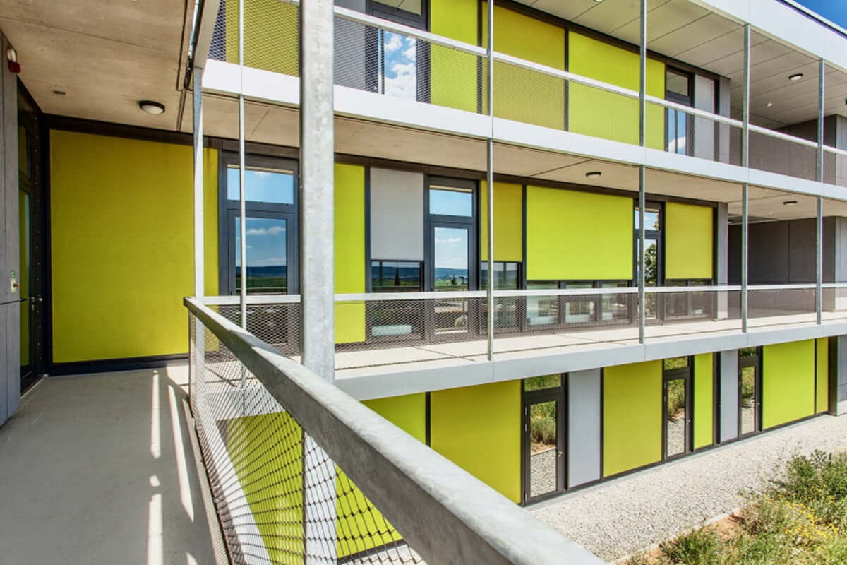 Modern building with large windows and green roller shades, showcasing stylish outdoor design.