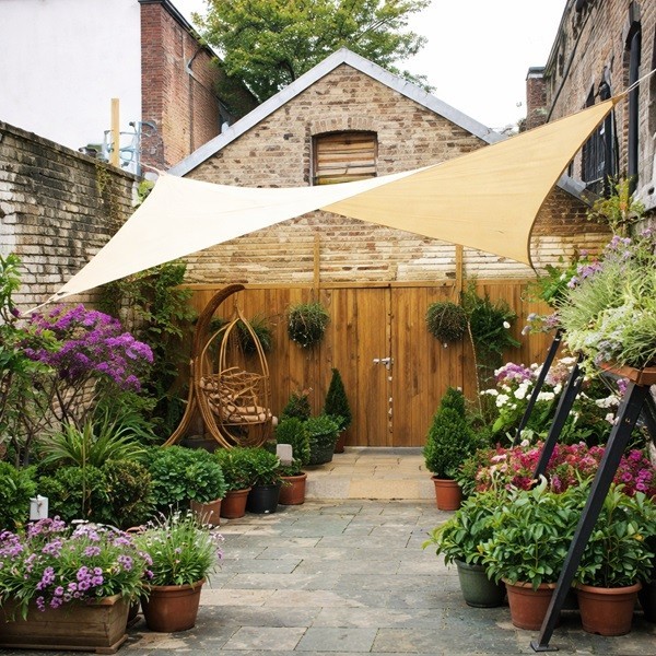 Voile d’ombrage beige tendue au-dessus d’une cour fleurie